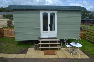um barracão verde com uma porta, uma mesa e cadeiras em Peaceful Shepherd's Hut next to Horse Field em Morpeth