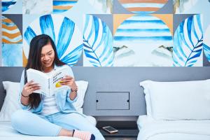 a woman sitting on a bed reading a book at Ibis Budget Singapore Sapphire in Singapore