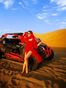 Dunhuang Vivian Desert Camping في دونهوانغ: امرأة في ثوب احمر جالسة على تلفزيون في الصحراء
