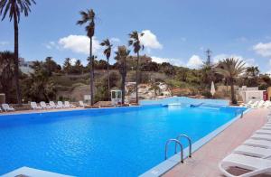 a large swimming pool with chairs and palm trees at Cresta Beach Studios in St. Julianʼs