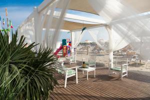 een terras met witte stoelen en een zandbak op het strand bij Hotel Castellucci in Bellaria-Igea Marina