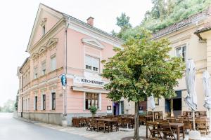 różowy budynek ze stołami i drzewem przed nim w obiekcie Erzherzog Johann Relax Appartements w mieście Ehrenhausen