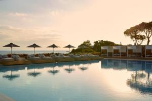 a swimming pool with chairs and umbrellas on the beach at Vincci EverEden in Anavyssos