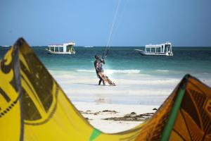 a man kite surfing on the beach with boats at Coconut Village Beach Resort in Diani Beach