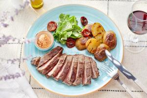 a blue plate with meat potatoes and vegetables on a table at Vincci EverEden in Anavyssos