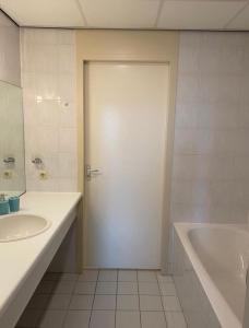 een badkamer met een witte deur, een wastafel en een bad bij Appartement Makkum aan het strand in Makkum