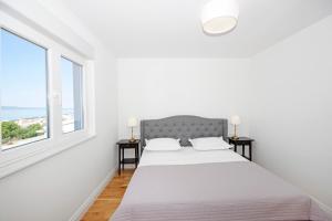 a white bedroom with a bed and two windows at Villa Edita in Makarska