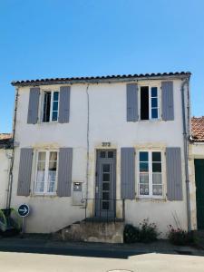 a white house with gray shutters on a street at L'Olivier de Milou in Le Bois-Plage-en-Ré