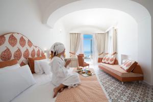 una mujer sentada en una cama en una habitación de hotel en CASA CAPRILE POSITANO, en Positano