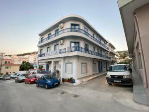 un bâtiment blanc avec des voitures garées dans un parking dans l'établissement Blue Sky Apartments, à Karpathos