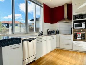 a kitchen with white cabinets and a red wall at Close To The Lake in Taupo