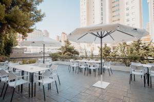 a patio with white tables and chairs and umbrellas at Luxmar Apartaments By MC in Benidorm