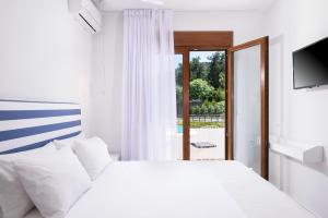 a white bedroom with a bed and a window at Villa Victoria by La Scala Beach in Limenas