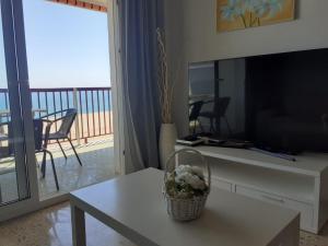 una sala de estar con TV y una mesa con flores. en Suitur apartamento primera linea mar vistas playa, en Canet de Mar