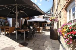 um pátio exterior com mesas, cadeiras e um guarda-sol em The Saracens Head Hotel em Highworth