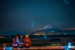 three people sitting on a wall looking at a mountain at night at The Secret Garden Cotopaxi in Hacienda Porvenir