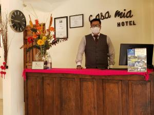 un hombre con una máscara de cara de pie detrás de un mostrador en Hotel Casa Mia en San Cristóbal de Las Casas