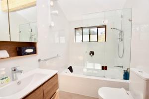 baño blanco con ducha y lavamanos en Sublime Cedar Lodge Leura, en Leura