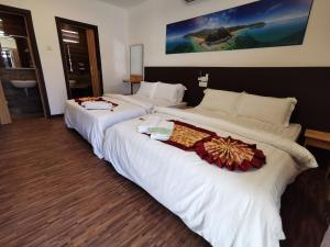 two beds in a hotel room with white sheets at The Barat Tioman Beach Resort in Kampong Juara