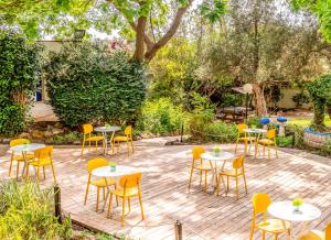 un patio con mesas blancas y sillas amarillas en Travel Hotel Gesher Haziv, en Gesher HaZiw