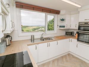a kitchen with white cabinets and a large window at Little Valley View in Hayle