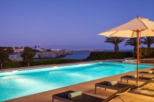 a swimming pool with an umbrella and chairs at Villa Rocamar in Cala en Blanes