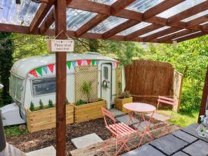a caravan with a table and chairs under a pergola at Cosy private Glamping with Pizza stove, Big Projector Screen, own hot Monsoon shower, breakfast - Glamping with a difference! in Tenby