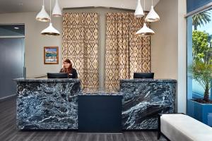 a woman sits at a reception desk in a lobby with marble counters at Elan Hotel in Los Angeles