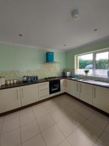 a large kitchen with green walls and white cabinets at HOMELY YELLOW BUNGALOW -Articlave-near Castlerock in Castlerock
