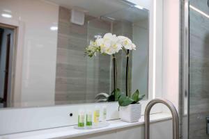 a bathroom sink with a mirror and a vase of flowers at AlphaPlus Apartment 91 in Abuja