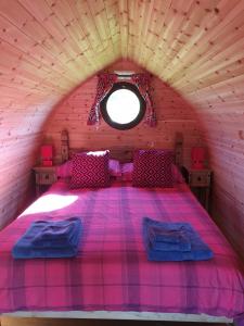a pink bed in a wooden room with a window at Woodbatch Camping & Glamping in Bishops Castle