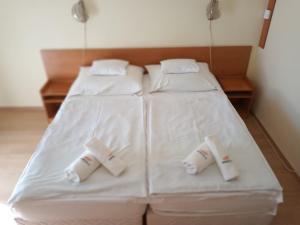 2 camas en una habitación con sábanas y almohadas blancas en Pergola Panzió, en Balatonföldvár