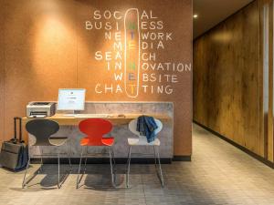 a desk with two chairs and a computer on a wall at ibis Hotel München Garching in Garching bei München