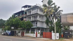 a tall white building with a palm tree in front of it at Seals Harbor Hotel in Weligama