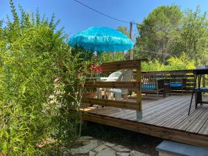 a wooden deck with a blue umbrella and chairs at studio indépendant dans villa avec piscine jacuzzi in Vidauban