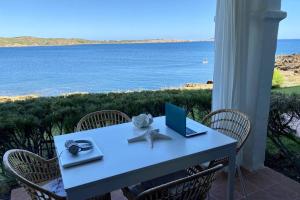 a table with a laptop and chairs with a view of the ocean at Miravent Terraza y Jardin Frente al mar Menorca in Fornells