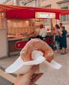 una mano sosteniendo una rosquilla delante de un carro de comida en Piazza Napoleone Sweet apartment, en Lucca