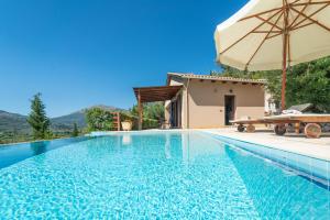 a swimming pool with an umbrella and a house at Kerithra Villa in Vasiliki