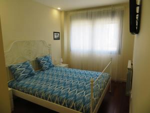 a bedroom with a bed with a blue comforter and a window at Coqueto apartamento Las Margas Golf in Sabiñánigo