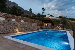 a swimming pool in front of a stone wall at Exclusive Villa Almissa with swimming pool and sea view in Lokva Rogoznica