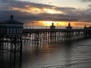 a pier with the sun setting in the water at Woodlands Holiday Apartments in Lytham St Annes