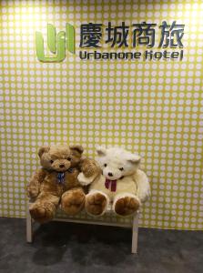 two teddy bears sitting on a bench in front of a wall at Urbanone Hotel in Taipei
