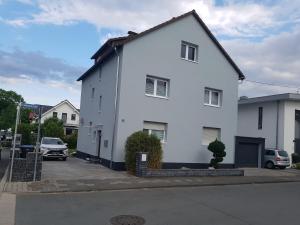 une maison blanche avec des voitures garées dans un parking dans l'établissement Ferienwohnung Rhein-Main, à Flörsheim am Main