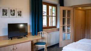 1 dormitorio con TV, escritorio y cama en Der Almhof, en Maria Alm am Steinernen Meer