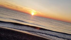 a sunset over the ocean with a person walking on the beach at EMI Apartamenty in Świnoujście