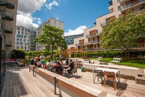 un groupe de personnes assises à des tables sur une terrasse en bois dans l'établissement Apparthotel Le Hüb Grenoble, à Grenoble