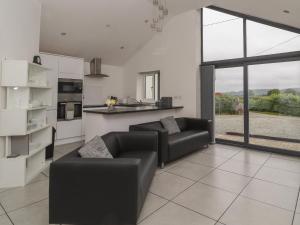 uma sala de estar com dois sofás pretos e uma cozinha em Cartrefle Fach em Pentraeth