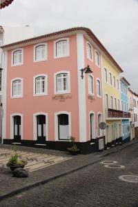 um edifício rosa e amarelo numa rua de calçada em Hotel Zenite em Angra do Heroísmo