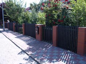 a black fence next to a sidewalk with red roses at Spacerkiem do plaży in Kołobrzeg