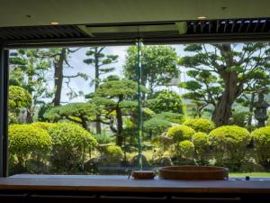 een raam met uitzicht op een tuin met bomen en struiken bij Hotel Flags Isahaya Nagasaki in Isahaya